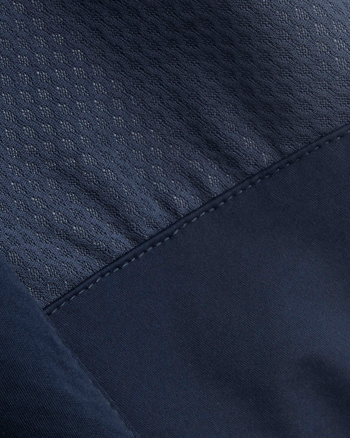 Close-up detail of a dark navy blue garment showing two different fabric textures: a textured mesh-like upper panel and a smoother lower panel with matching dark stitching.
