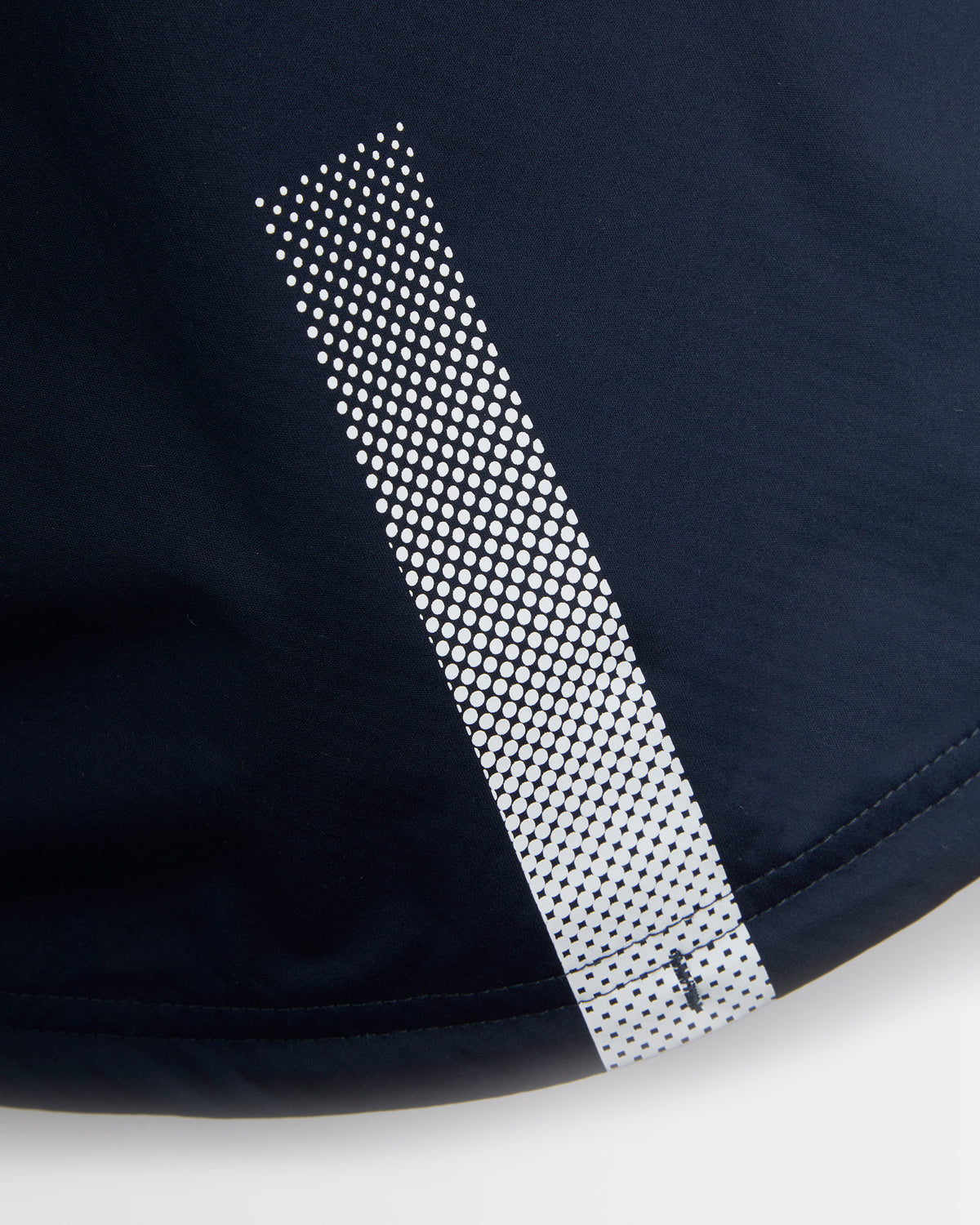 Close-up of dark navy athletic fabric with a vertical reflective-looking strip made of repeating white dots, shown against a light neutral background.