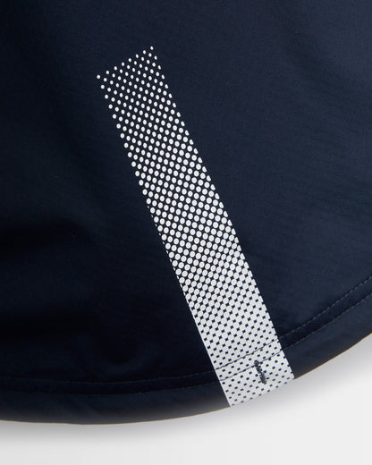 Close-up of dark navy athletic fabric with a vertical reflective-looking strip made of repeating white dots, shown against a light neutral background.