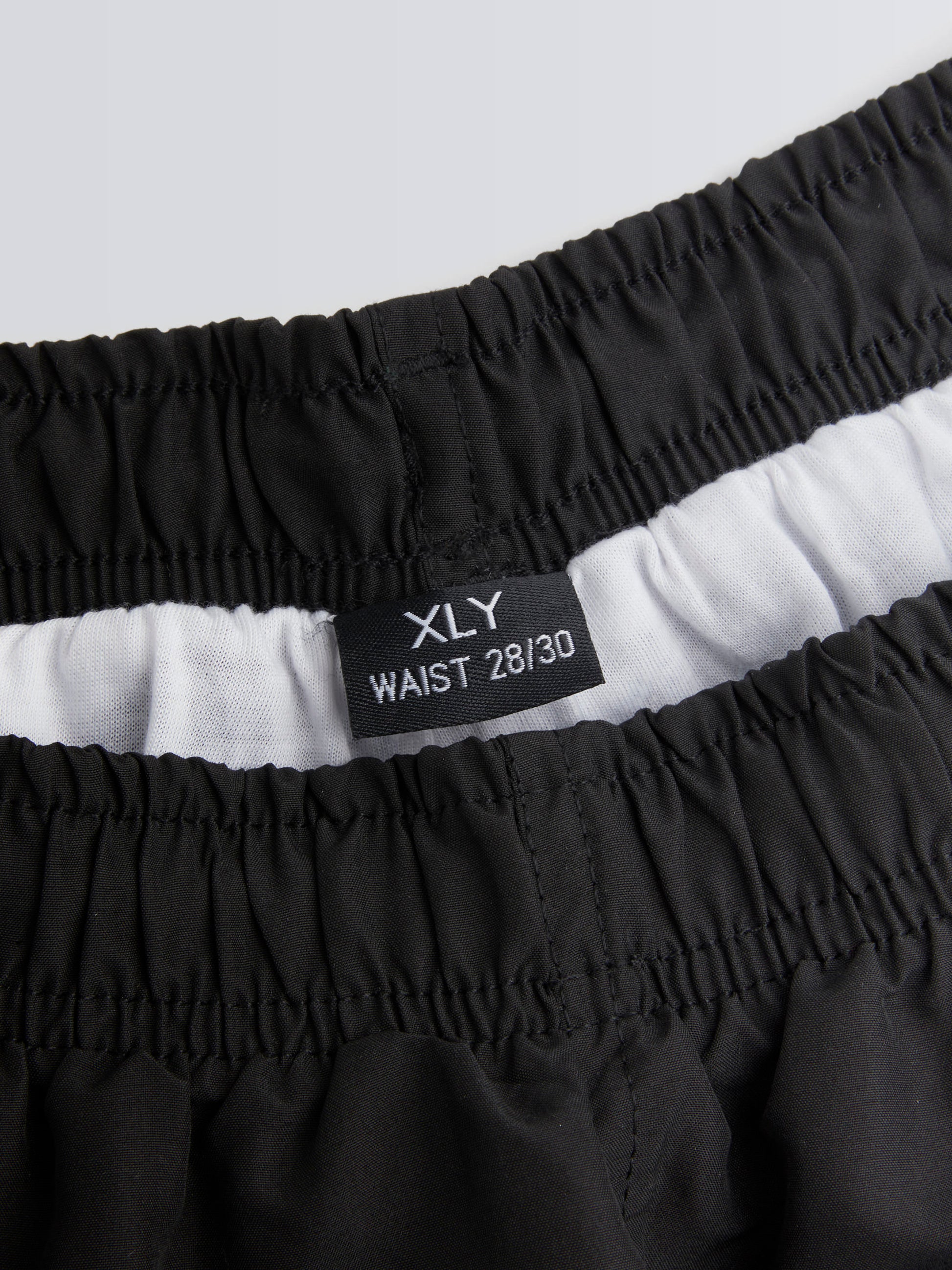 Black shorts with waistband label on a light grey background