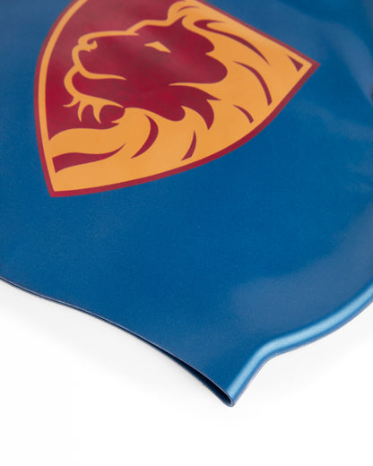 Close-up of a blue product surface featuring a large shield-shaped lion head logo in maroon and gold, photographed on a white background.