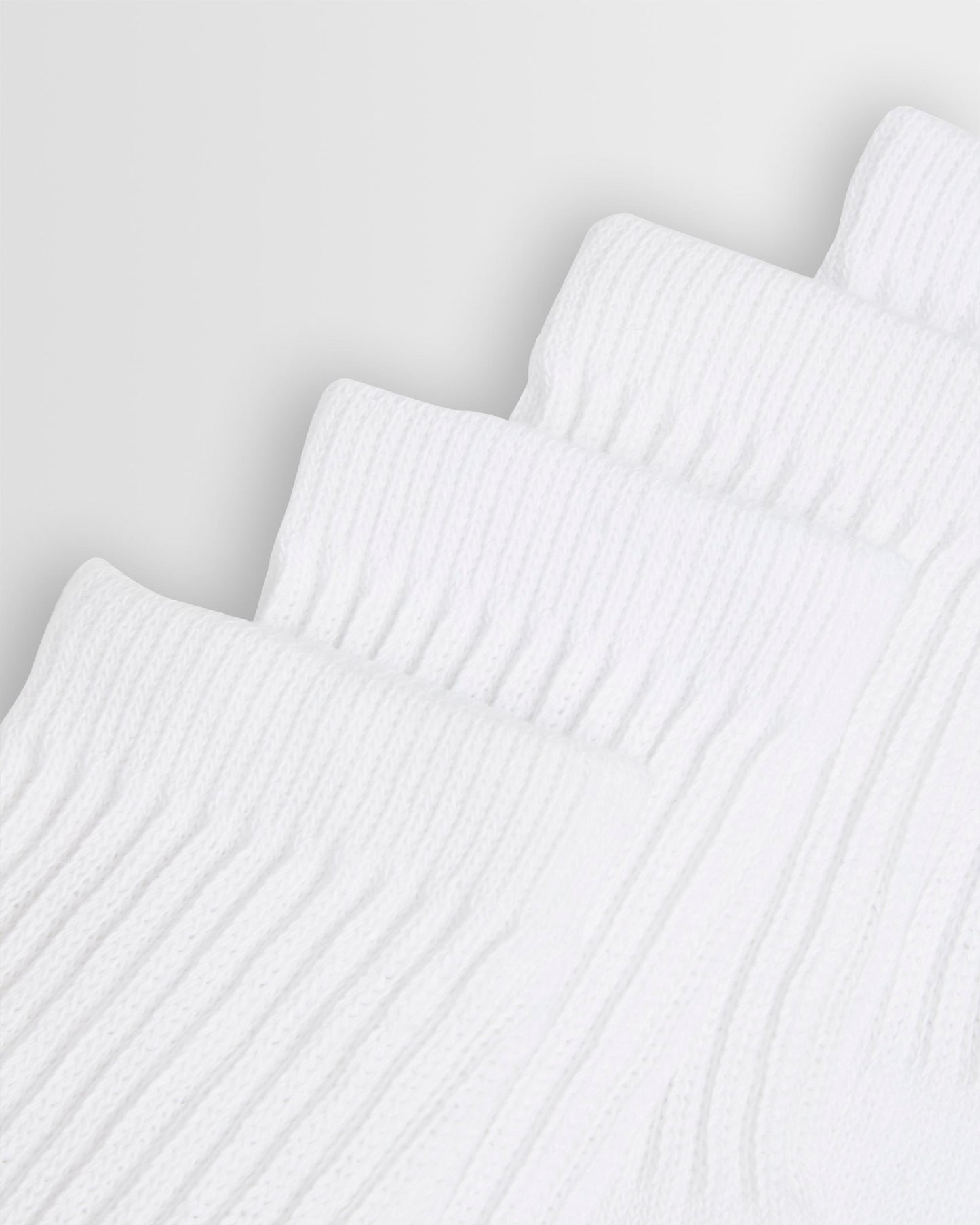 Close up of the top of white sports socks stacked on top of each other against a light background.