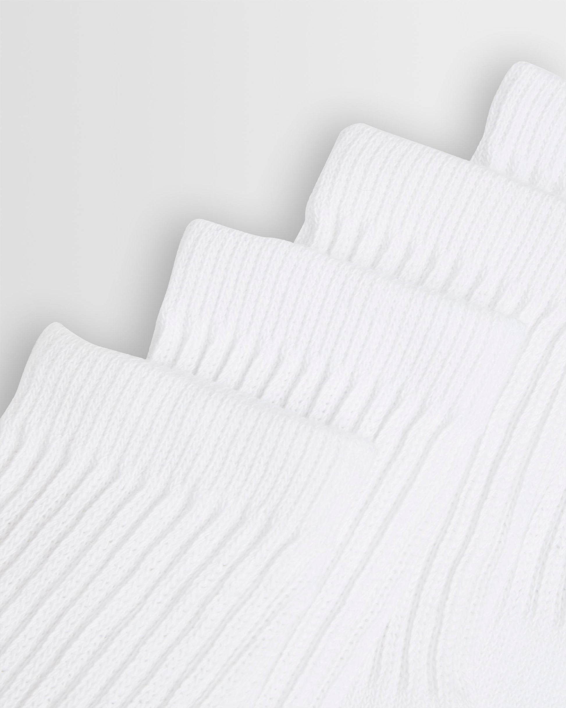 Close up of the top of white sports socks stacked on top of each other against a light background.