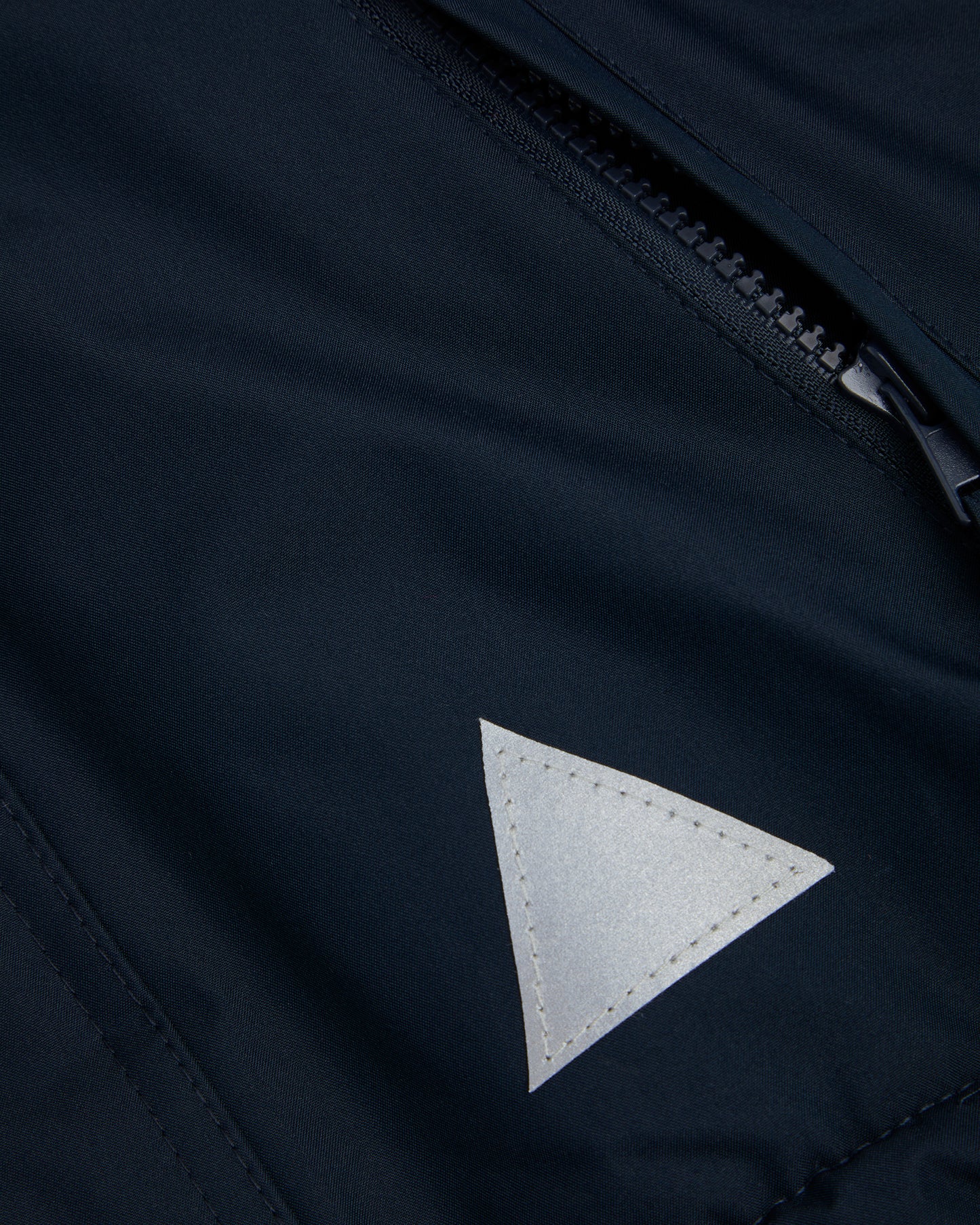 Close up of A navy-colored, waterproof coat front zip pocket and reflective triangle on the front left.