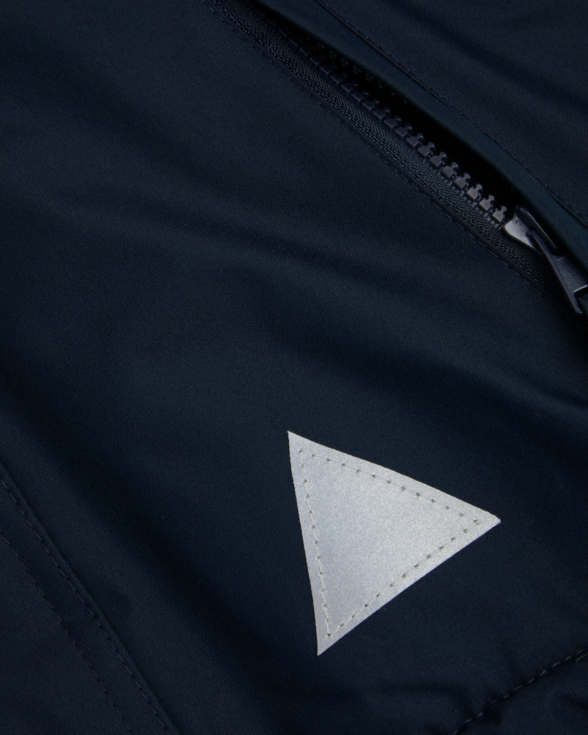 Close up of A navy-colored, waterproof coat front zip pocket and reflective triangle on the front left.