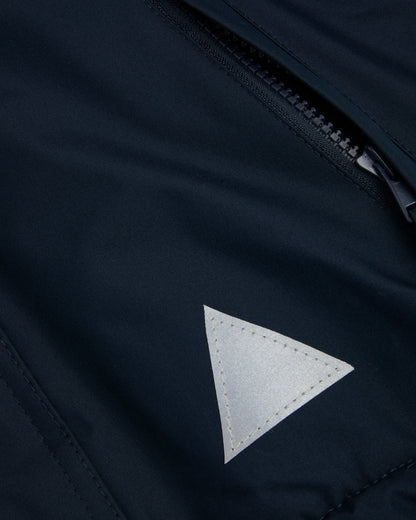 Close up of A navy-colored, waterproof coat front zip pocket and reflective triangle on the front left.